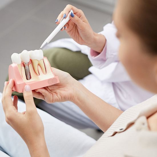 A dentist showing a patient a dental implant model