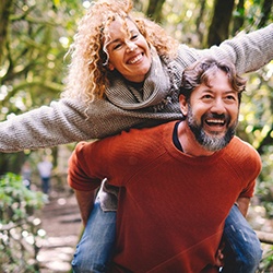Woman with curly hair riding piggy back on man wearing red orange sweater