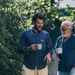 Two men in blue shirts holding coffee cups outside talking