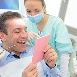 Man in blue shirt smiling at reflection with dentist looking over his shoulder