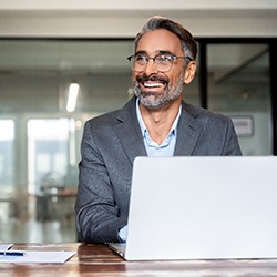 Man in gray suit at work on laptop smiling