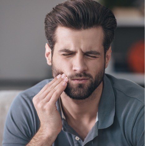 Man wincing and holding his cheek in pain