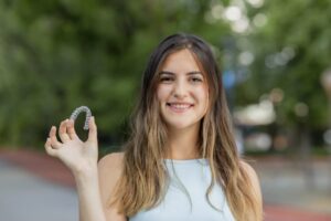 Smiling woman holding her Invisalign aligner while standing outside