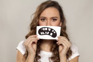 Woman holding a drawn cartoon style frowning mouth with missing teeth in front of her face