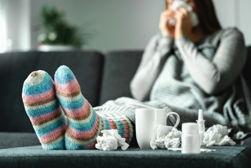 Woman on couch blowing her nose and surrounded by used tissues because of allergies